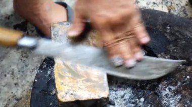 Yaşlı bir adam bir bıçağı bilemek için ıslak taş kullanıyor. Geleneksel Tayland usulü keskin bir bıçak yapmak onu bilenen bir taşa ileri geri sürmeyi gerektirir. Bıçağı el yağmuruna tut..