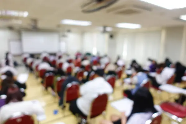 Blurred abstract background of examination room with undergraduate students inside. Blurred view of a student doing the final test in the exam room. Blurry view of study chairs in university.