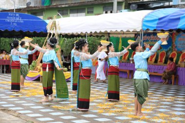 Lampang, Tayland - 7 Kasım 2024: Geleneksel Tayland kıyafetleri içinde bir grup Asyalı kadın ve erkek Ngao Köprüsü 'nde Tanrı' ya Çiçek Veren Sarı Çiçekler Festivali 'nde dans ediyor.