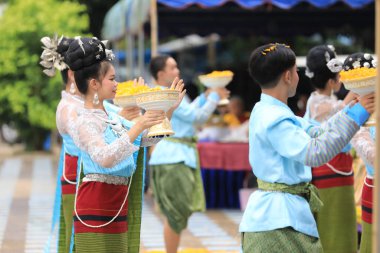Lampang, Tayland - 7 Kasım 2024: Geleneksel Tayland kıyafetleri içinde bir grup Asyalı kadın ve erkek Ngao Köprüsü 'nde Tanrı' ya Çiçek Veren Sarı Çiçekler Festivali 'nde dans ediyor.
