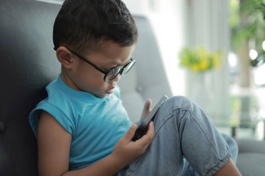 Çocuk kanepede oyun oynuyor, çocuklar telefon kullanıyor. 