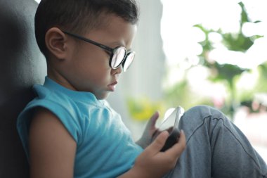 Çocuk kanepede oyun oynuyor, çocuklar telefon kullanıyor. 