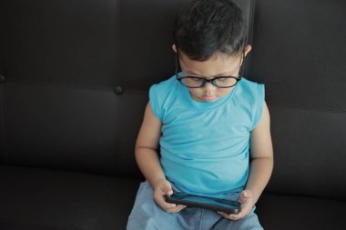 Çocuk kanepede oyun oynuyor, çocuklar telefon kullanıyor. 