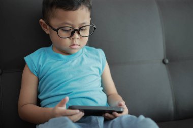 Çocuk kanepede oyun oynuyor, çocuklar telefon kullanıyor. 