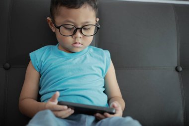 Çocuk kanepede oyun oynuyor, çocuklar telefon kullanıyor. 