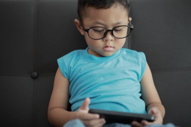 Çocuk kanepede oyun oynuyor, çocuklar telefon kullanıyor. 