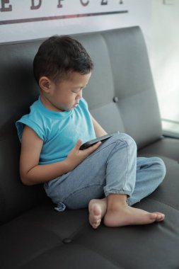 Çocuk kanepede oyun oynuyor, çocuklar telefon kullanıyor. 