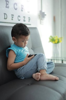 Çocuk kanepede oyun oynuyor, çocuklar telefon kullanıyor. 