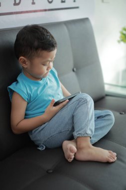 Çocuk kanepede oyun oynuyor, çocuklar telefon kullanıyor. 