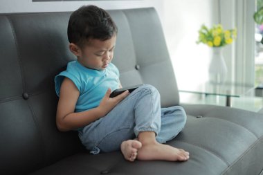 Çocuk kanepede oyun oynuyor, çocuklar telefon kullanıyor. 