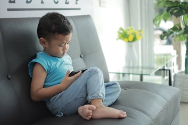 Çocuk kanepede oyun oynuyor, çocuklar telefon kullanıyor. 