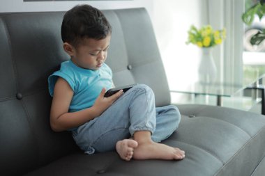 Çocuk kanepede oyun oynuyor, çocuklar telefon kullanıyor. 