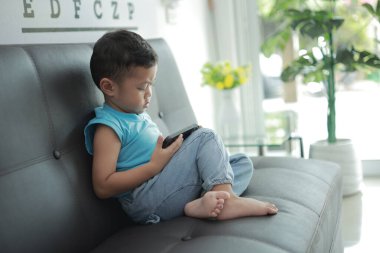 Çocuk kanepede oyun oynuyor, çocuklar telefon kullanıyor. 