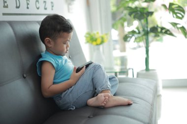 Çocuk kanepede oyun oynuyor, çocuklar telefon kullanıyor. 