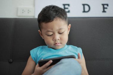 Çocuk kanepede oyun oynuyor, çocuklar telefon kullanıyor. 