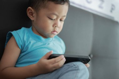 Çocuk kanepede oyun oynuyor, çocuklar telefon kullanıyor. 