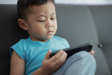 Çocuk kanepede oyun oynuyor, çocuklar telefon kullanıyor. 