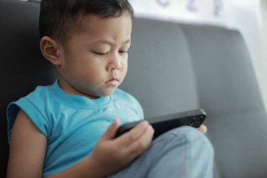 Çocuk kanepede oyun oynuyor, çocuklar telefon kullanıyor. 