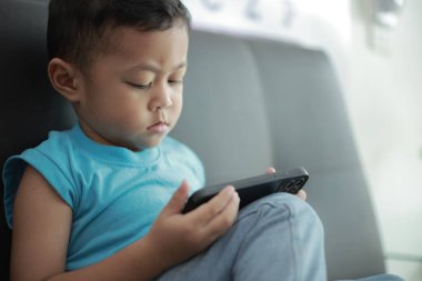 Çocuk kanepede oyun oynuyor, çocuklar telefon kullanıyor. 