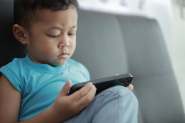 Çocuk kanepede oyun oynuyor, çocuklar telefon kullanıyor. 