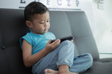 Çocuk kanepede oyun oynuyor, çocuklar telefon kullanıyor. 