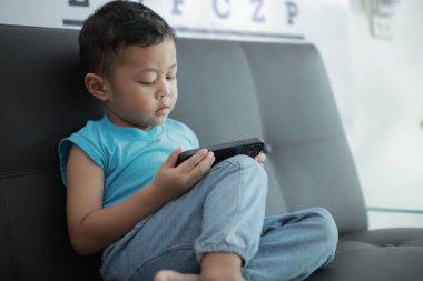 Çocuk kanepede oyun oynuyor, çocuklar telefon kullanıyor. 