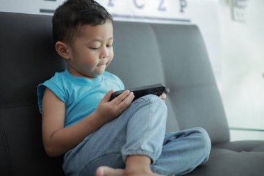 Çocuk kanepede oyun oynuyor, çocuklar telefon kullanıyor. 