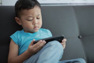 Çocuk kanepede oyun oynuyor, çocuklar telefon kullanıyor. 