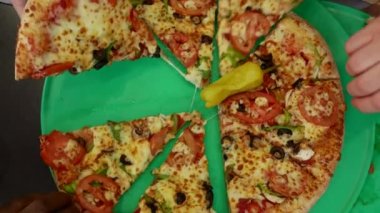 Yukarıdan gelen yeşil tepside elleriniz canlı vejetaryen pizza dilimlerine uzanırken nefis deneyimi yakalayın. Renkli karışım sizi lezzetli bir yemek anının tadını çıkarmaya davet ediyor.