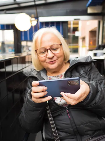 stock image blonde gamer grandmother with glasses out of focus enjoying playing on smartphone