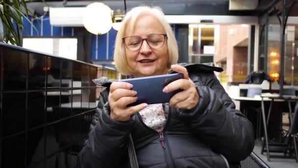 Rubia Gamer Abuela Con Gafas Jugando Teléfono Inteligente Café Pierde — Vídeo de stock