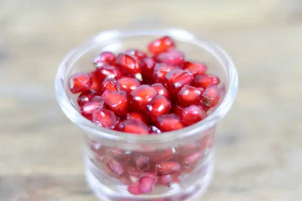 Red Pomegranate seeds on the wooden background. Fresh pomegranate close up picture on the wooden background. Healthful natural fruits for cancer patient. Open section of a pomegranate fruit exposing the ripe red seeds within.