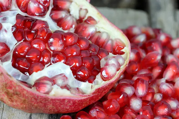 Red Pomegranate seeds on the wooden background. Fresh pomegranate close up picture on the wooden background. Healthful natural fruits for cancer patient. Open section of a pomegranate fruit exposing the ripe red seeds within.