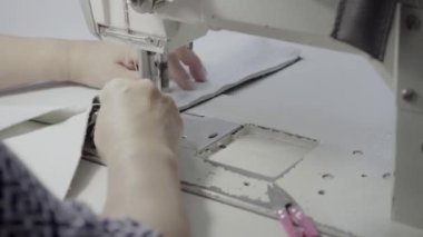 Atölyedeki terzi dikiş makinesine beyaz iplikçikli, hakiki deriden yapılmış bir ürün dikiyor.