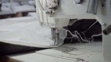 Atölyedeki terzi dikiş makinesine beyaz iplikçikli, hakiki deriden yapılmış bir ürün dikiyor.