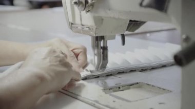 Atölyedeki terzi dikiş makinesine beyaz iplikçikli, hakiki deriden yapılmış bir ürün dikiyor.