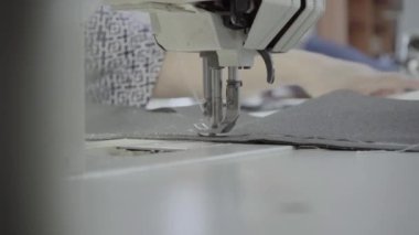 Atölyedeki terzi dikiş makinesine beyaz iplikçikli, hakiki deriden yapılmış bir ürün dikiyor.
