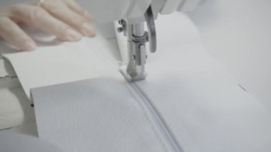 Atölyedeki terzi dikiş makinesine beyaz iplikçikli, hakiki deriden yapılmış bir ürün dikiyor.