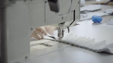 Atölyedeki terzi dikiş makinesine beyaz iplikçikli, hakiki deriden yapılmış bir ürün dikiyor.