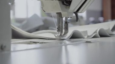Atölyedeki terzi dikiş makinesine beyaz iplikçikli, hakiki deriden yapılmış bir ürün dikiyor.