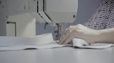 Atölyedeki terzi dikiş makinesine beyaz iplikçikli, hakiki deriden yapılmış bir ürün dikiyor.