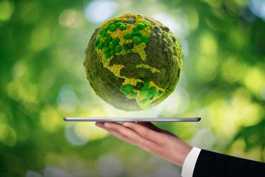 A man is holding a digital tablet. Above this green planet Earth. Symbol of sustainable development and renewable energy clipart