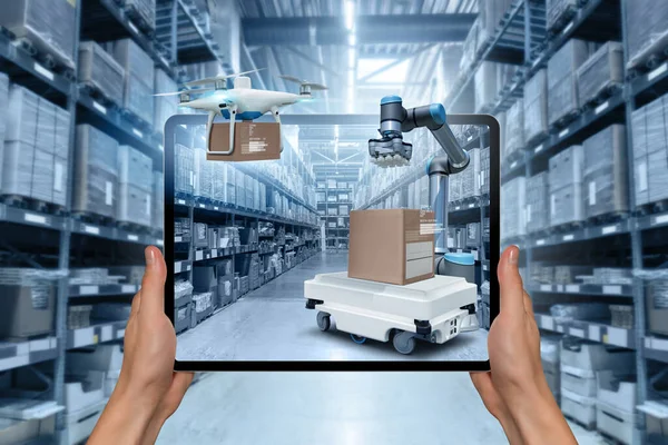 Warehouse manager with digital tablet controls robot and drone