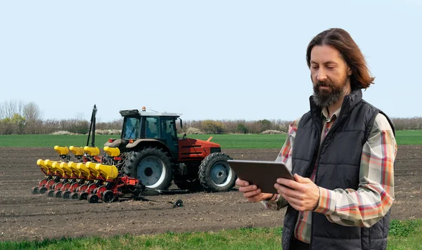 Farmer with a digital tablet on the background of an agricultural tractor with seeding machine