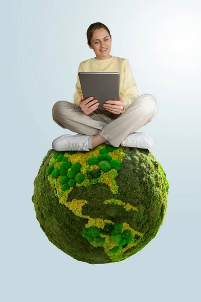 Woman with digital tablet sitting on green planet Earth. Concept of sustainable development and environmental education