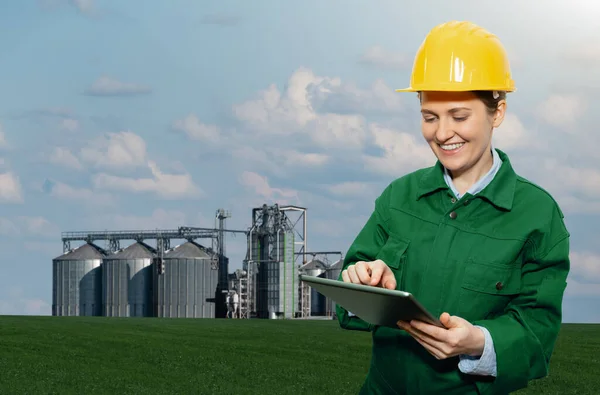 Woman engineer with a digital tablet on a background of agricultural silos for biofuel production