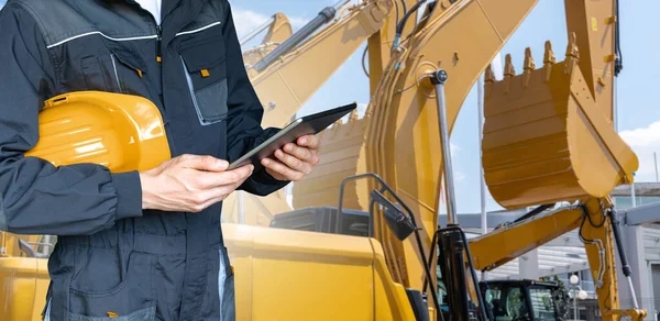 Engineer with helmet and digital tablet on the background of construction machines
