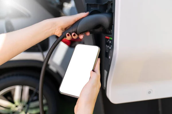 手与智能手机和充电插头在电动汽车的背景 白色屏幕 你可以在这里添加你的内容 高质量的照片 — 图库照片