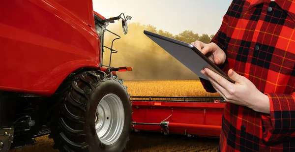 Farmer with digital tablet on a background of harvester. Smart farming concept. High quality photo