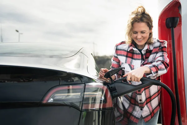 Ekose Gömlekli Bir Kadın Elektrikli Bir Arabayı Şarj Ediyor — Stok fotoğraf